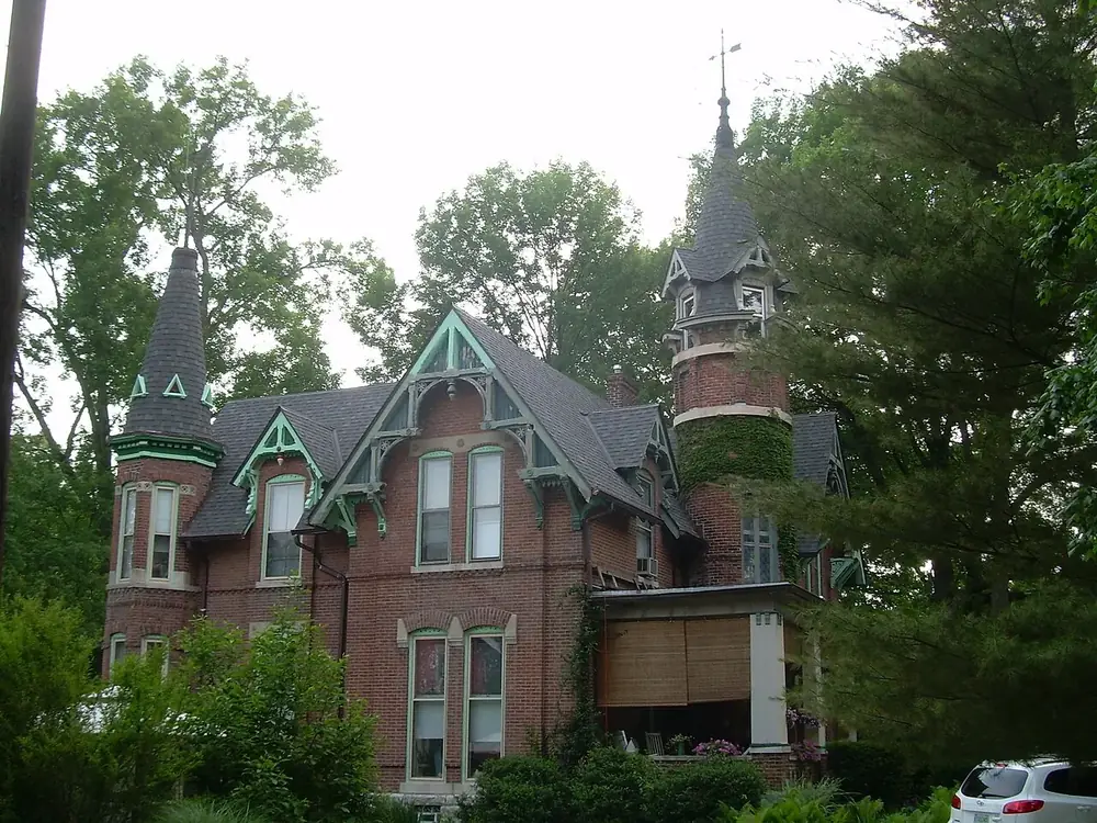 A brick Victorian house with a turret and gingerbread trim on a tree-lined street in Irvington, Indianapolis